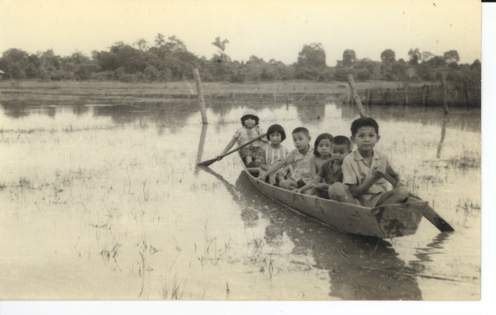 Children in a small wooden boat on flooded paddies, Laos